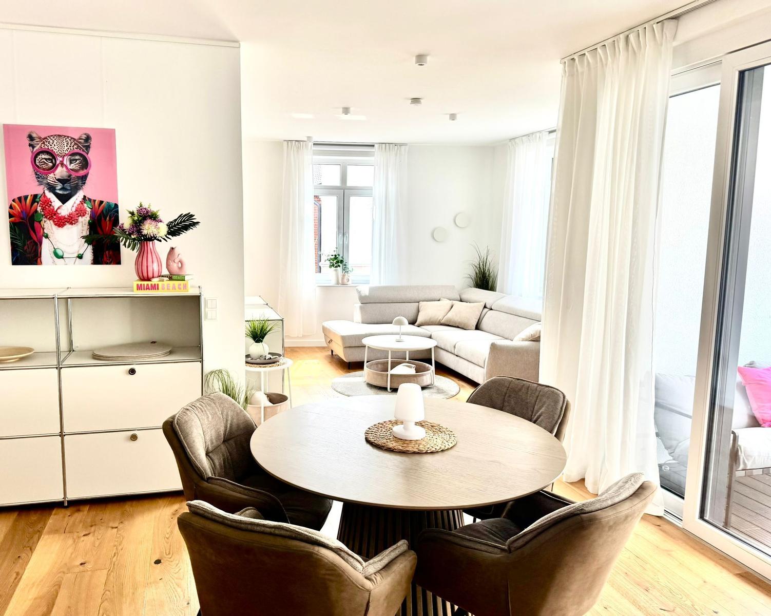 Essbereich mit runder Tisch und vier Stühlen. Wohnbereich mit Sofa und großen Fenstern.