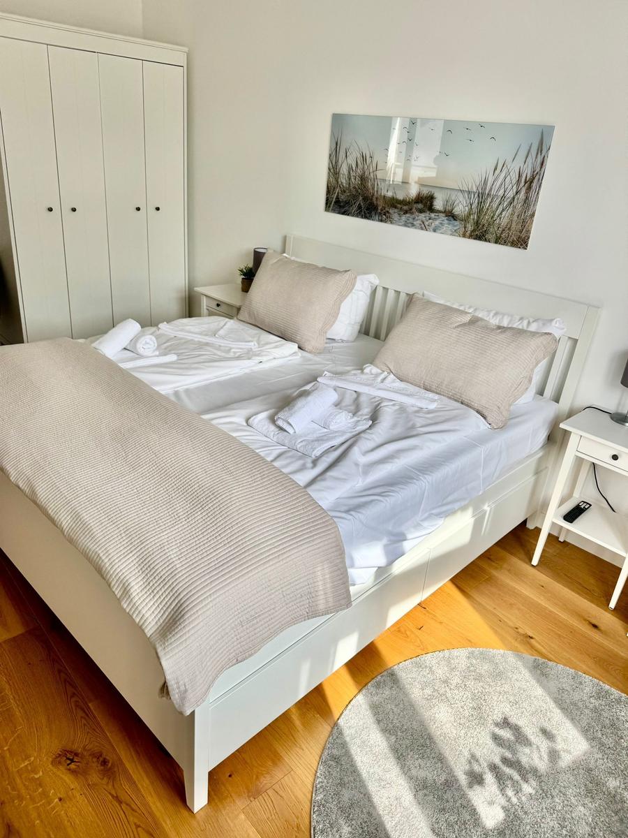 Schlafzimmer mit weißem Bett, Kleiderschrank und Wandbild.