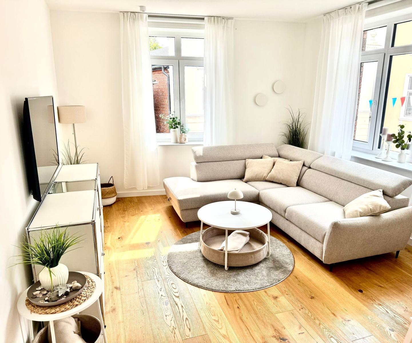 Wohnzimmer mit Ecksofa, runden Tisch und Holzboden.