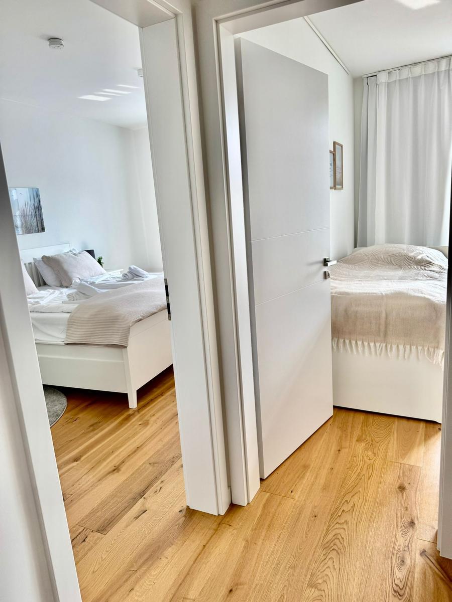 Zwei Schlafzimmer mit weißen Betten und Holzboden sichtbar durch Tür.