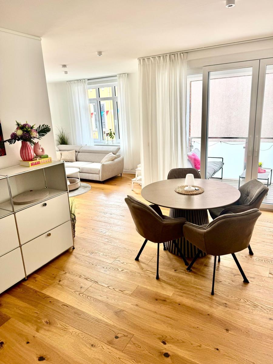 Ein Essbereich mit runden Tisch und Stühlen, daneben Wohnbereich mit Sofa und Balkon.