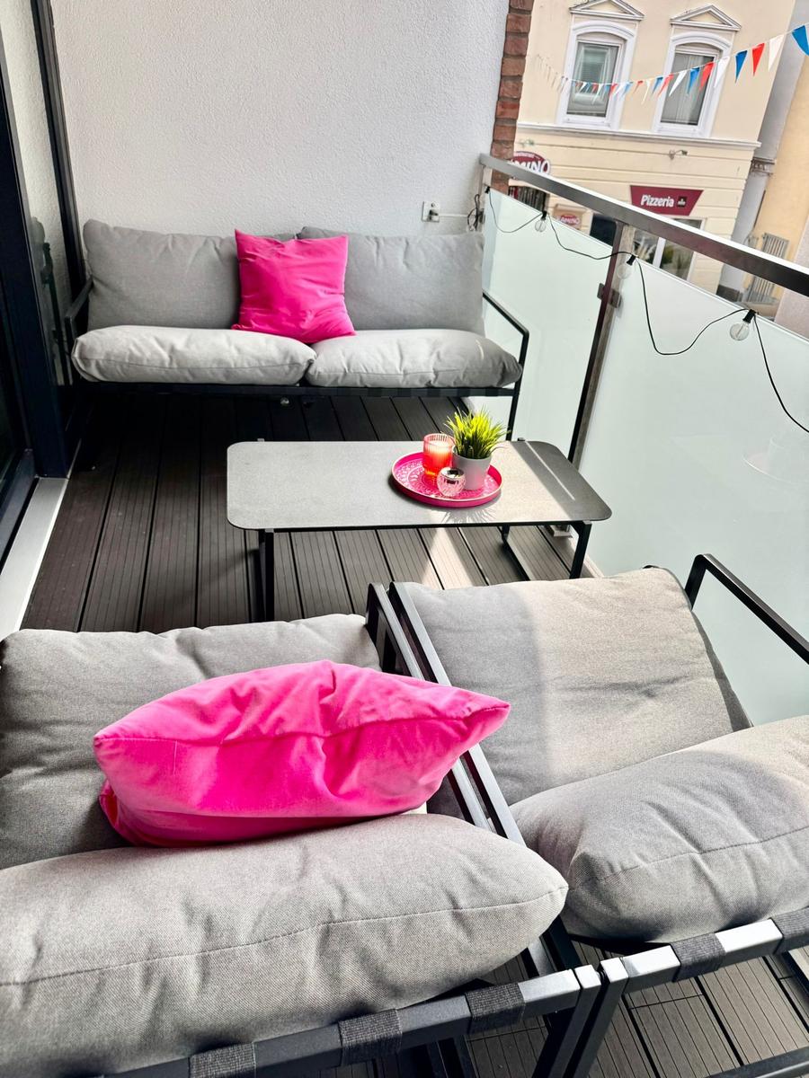 Terrasse mit Sofa, Sitzgruppe und Tisch. Pinker Kissen und Pflanze.