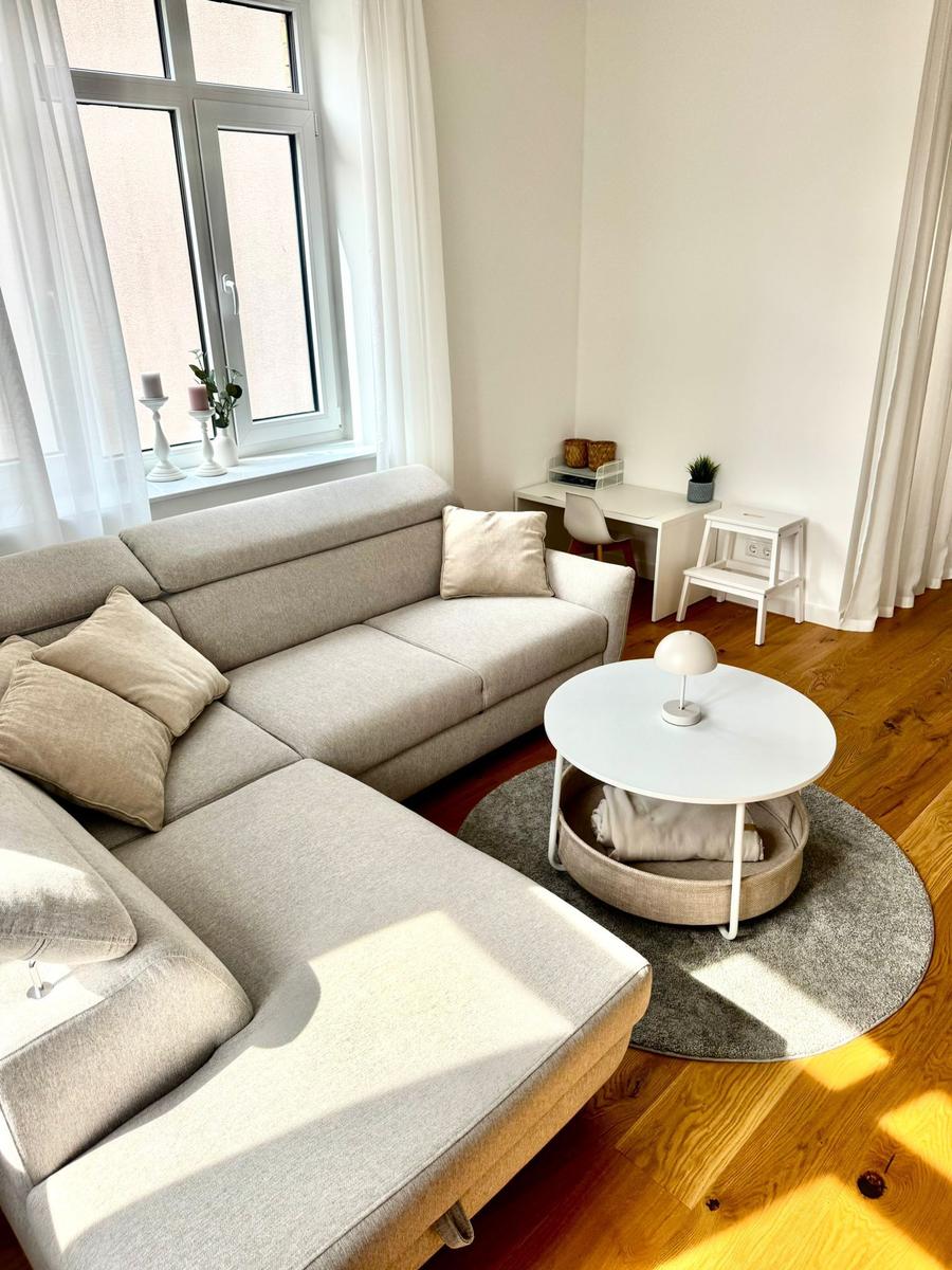 Ein Wohnzimmer mit grauem Sofa, runden Tisch und Holzboden.