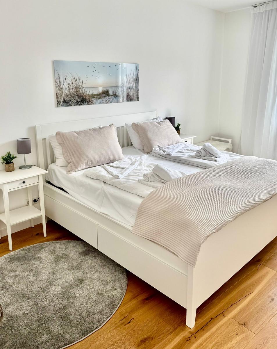 Schlafzimmer mit weißem Bett, Holzboden und Wandbild