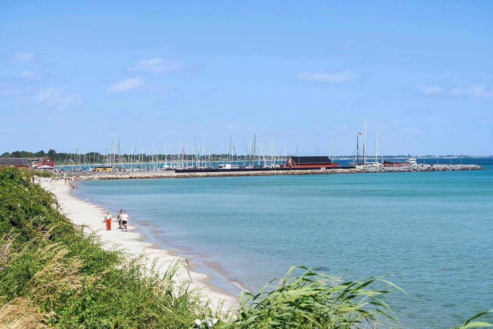 Strand mit Booten und klarem Wasser. Menschen spazieren entlang des Ufers.
