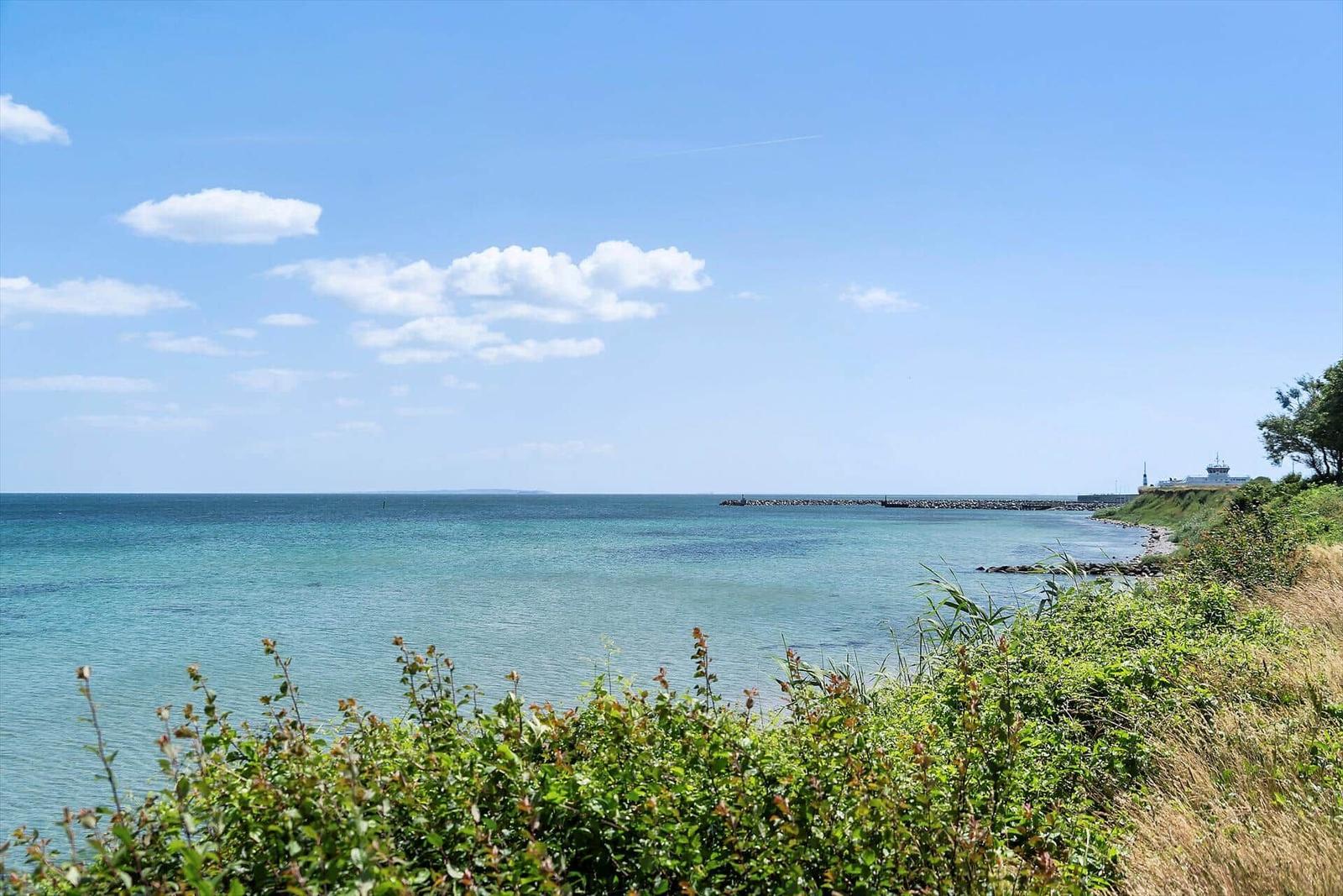 Meeresblick mit klarem Himmel und grüner Vegetation am Strand.
