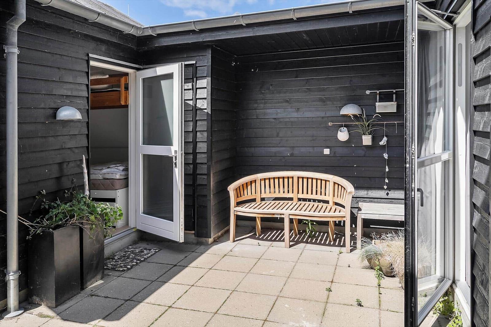 Gedeckter Außenbereich mit Holzbank, Pflanzen und offenen Türen zu Schlafzimmer.