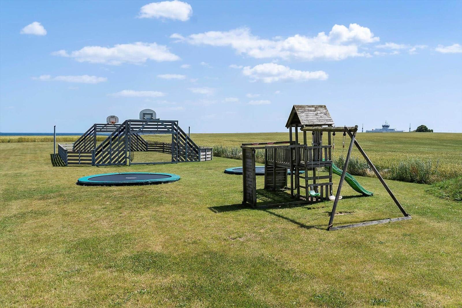 Großer Spielplatz mit Rutsche, Schaukel und Trampolin. Blick auf das Meer.