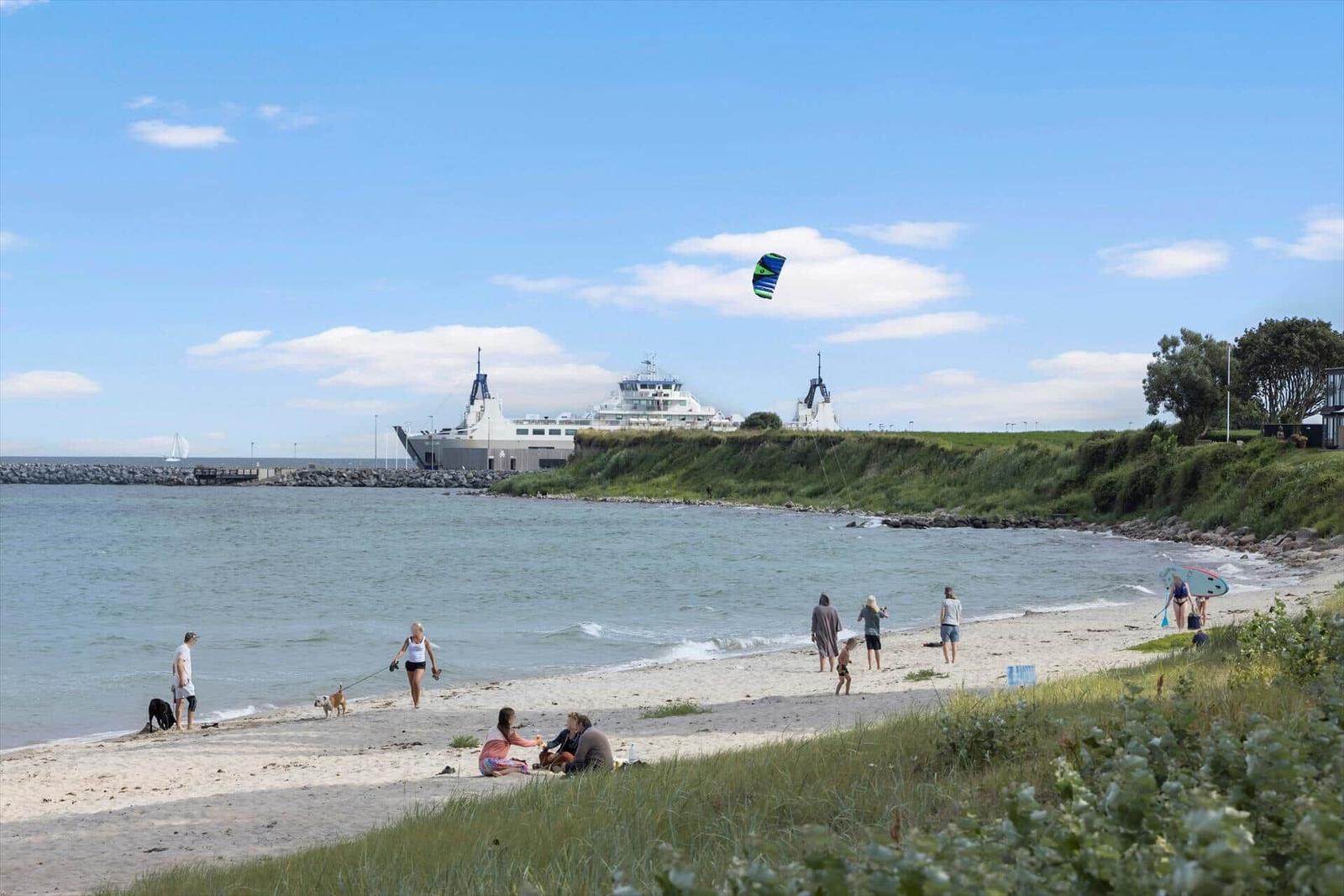 Strand mit Menschen, Kite und Fähre im Hintergrund.