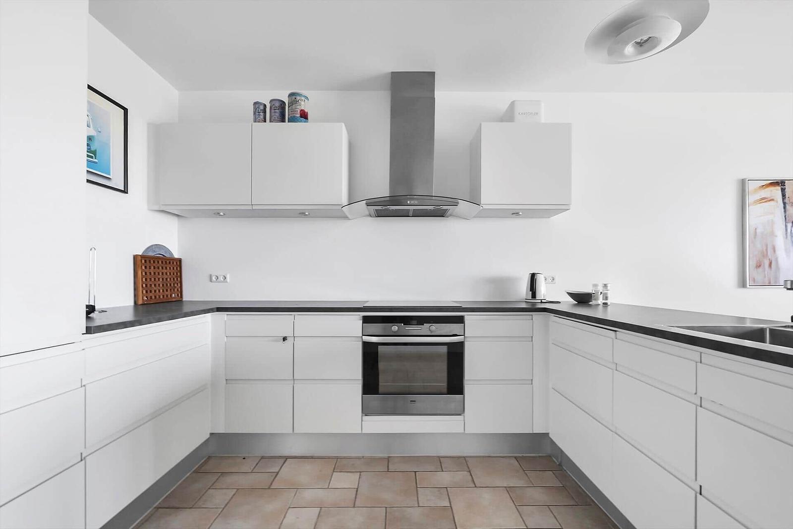 Moderne Küche mit weißen Schränken, Edelstahlherd und dunklem Arbeitsplatz.