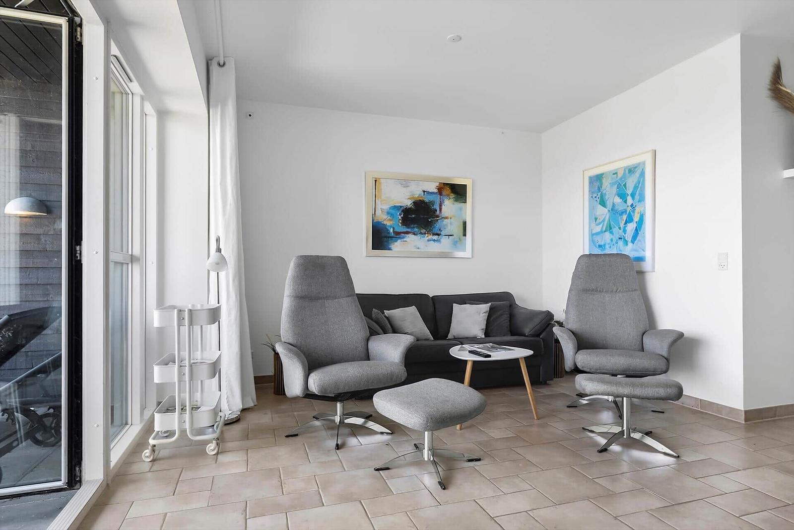 Wohnzimmer mit grauen Sesseln, Sofa und abstrakten Bildern an den Wänden.