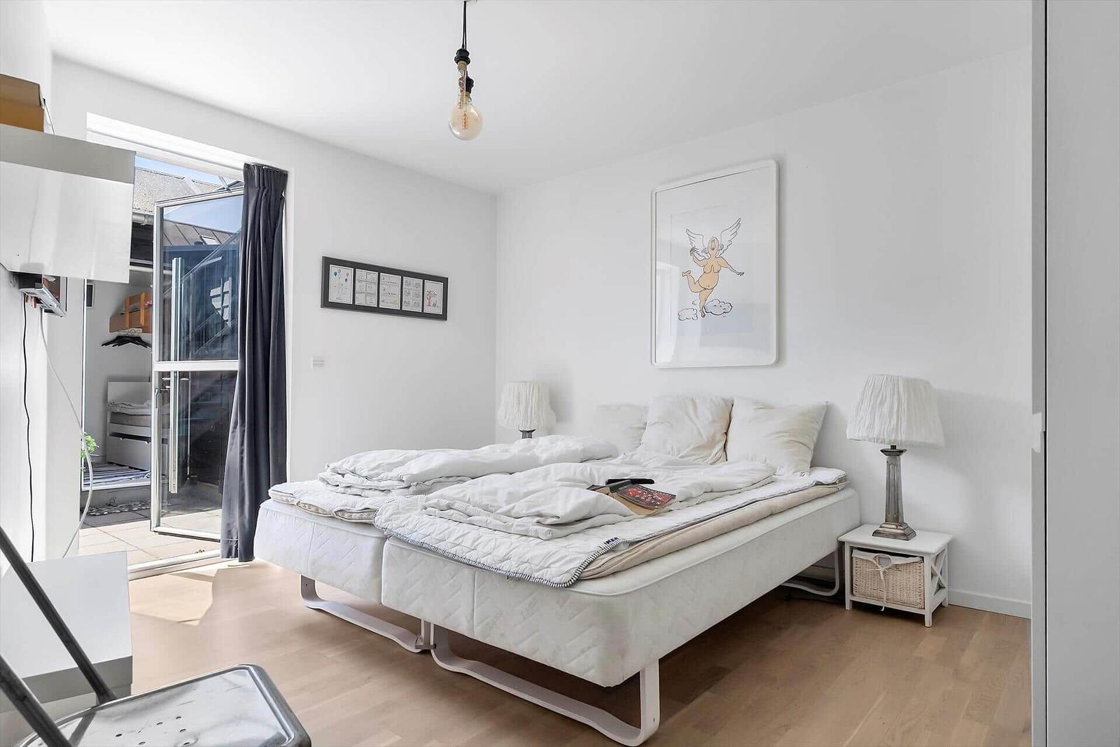 Schlafzimmer mit Doppelbett, Nachttisch und Fenster zur Terrasse.