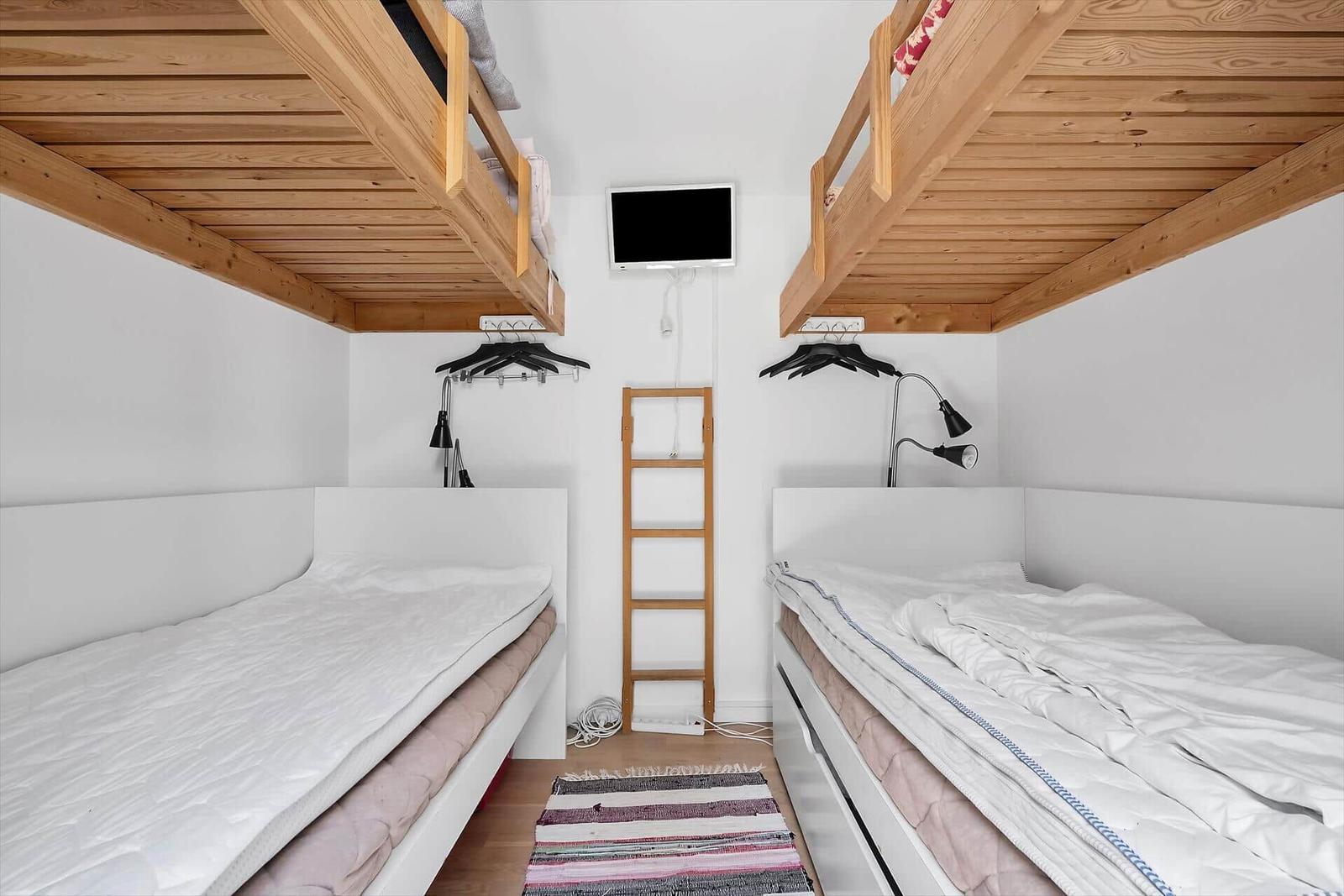 Zwei Etagenbetten mit Matratzen und Nachttischen. Zwischen ihnen steht eine Leiter.