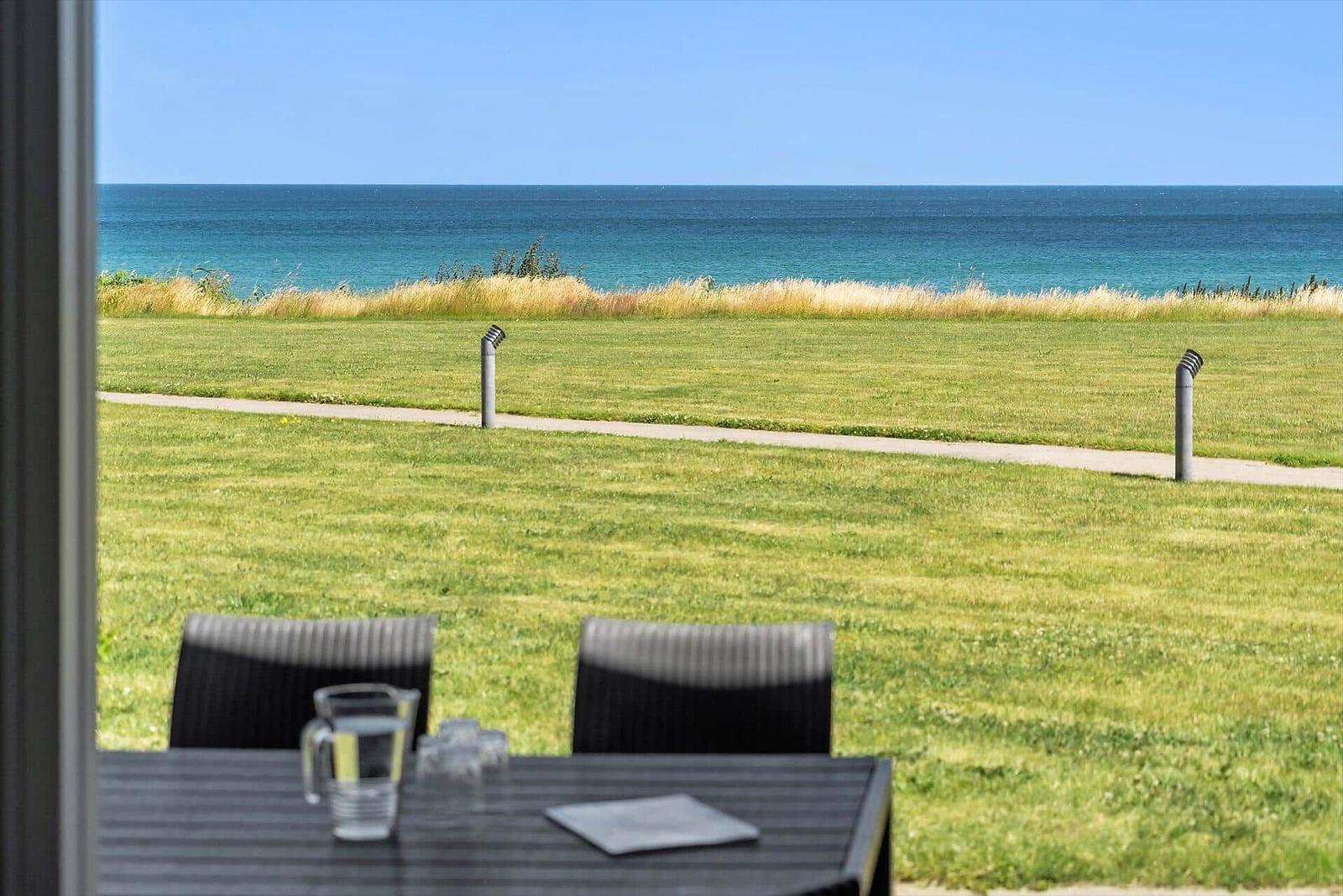 Terrasse mit Tisch und Stühlen. Blick auf Grasfläche und Meer.