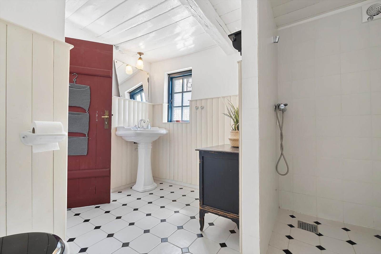 Badezimmer mit Standwaschbecken, Dusche und schwarz-weißem Fliesenboden.