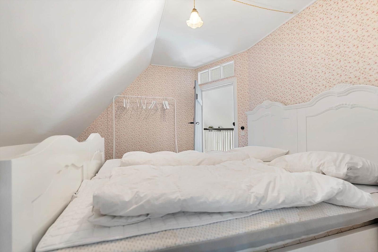 Schlafzimmer mit weißem Bett und gemusterter Wandtapete.