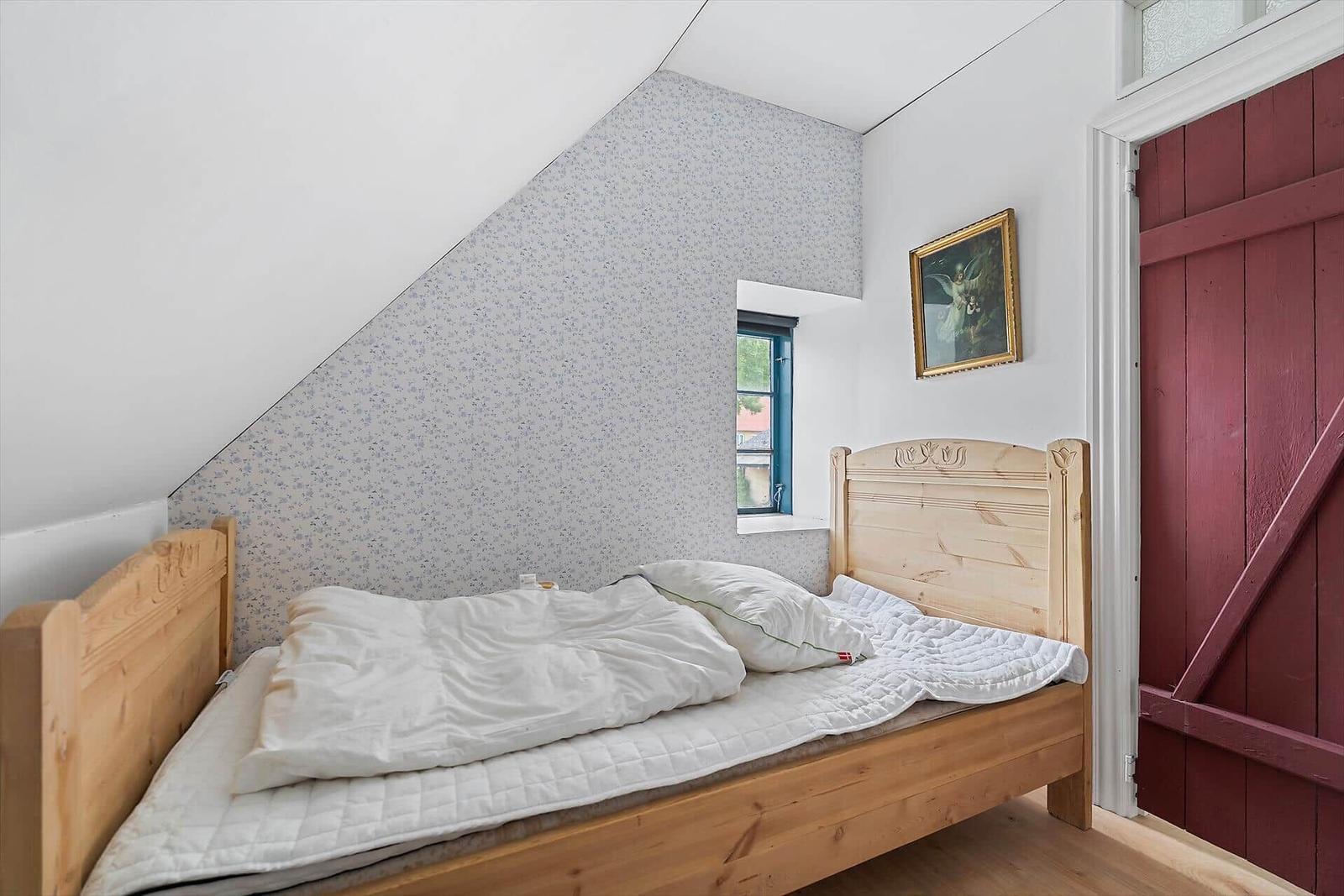 Ein Schlafzimmer mit Holzbett, gemusterter Wand und roter Tür.