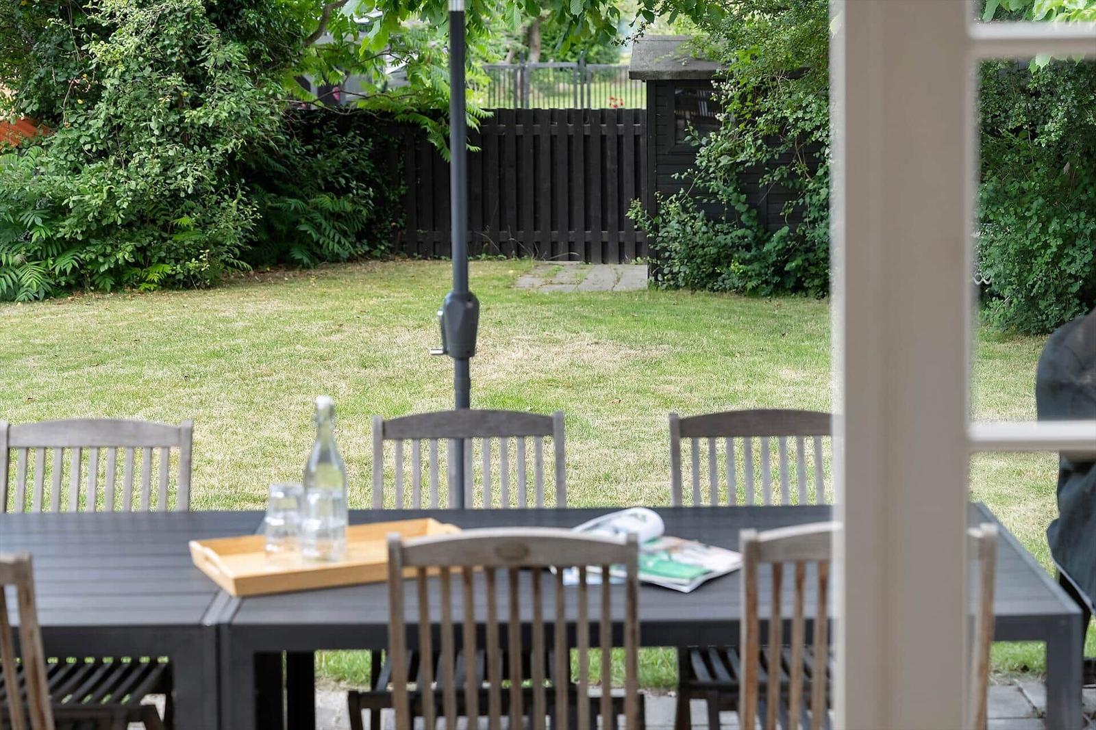 Außenbereich mit Tisch und Stühlen, Grasfläche und Gartenzaun im Hintergrund.
