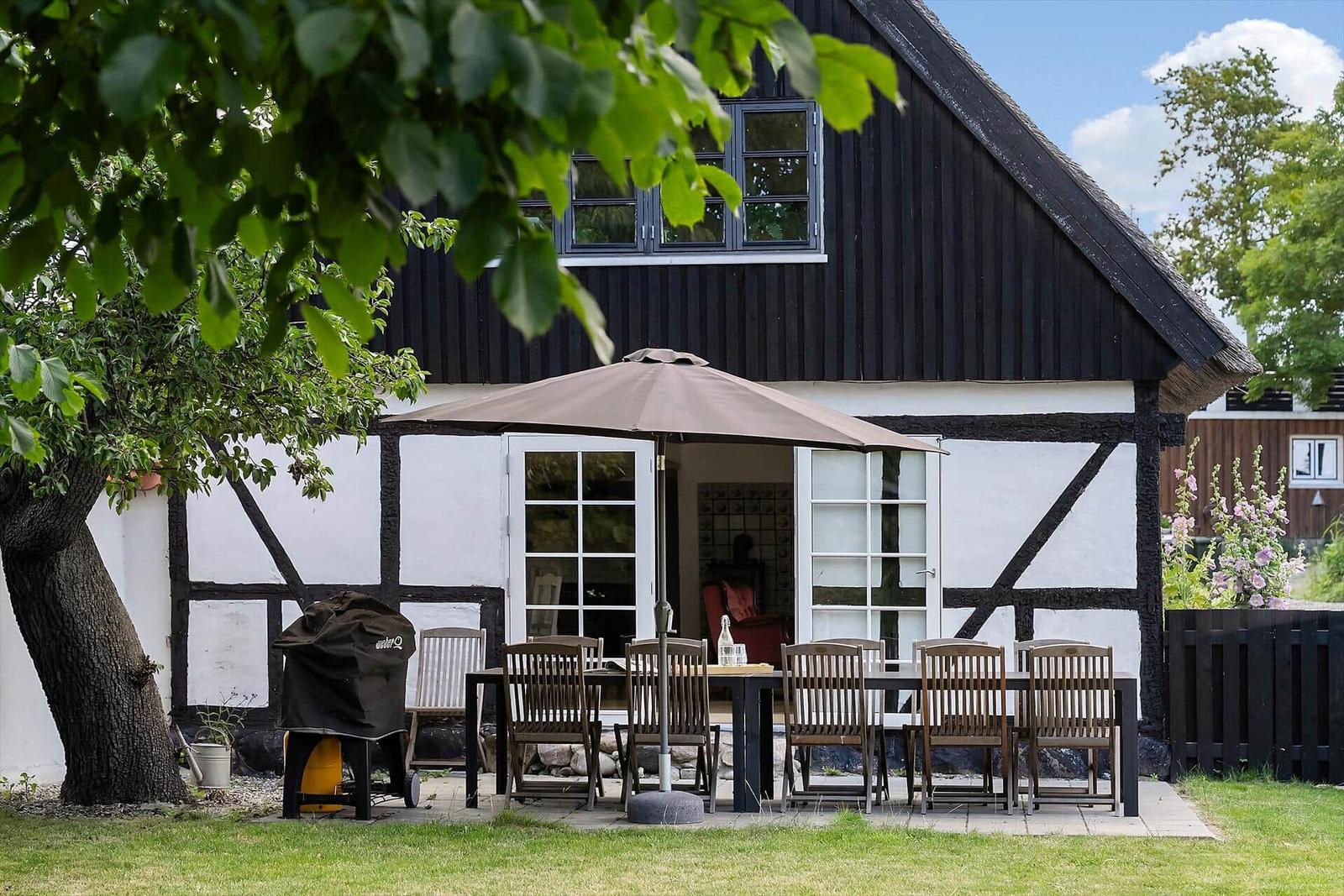 Terrasse mit Tisch, Stühlen und Sonnenschirm vor einem Fachwerkhaus.