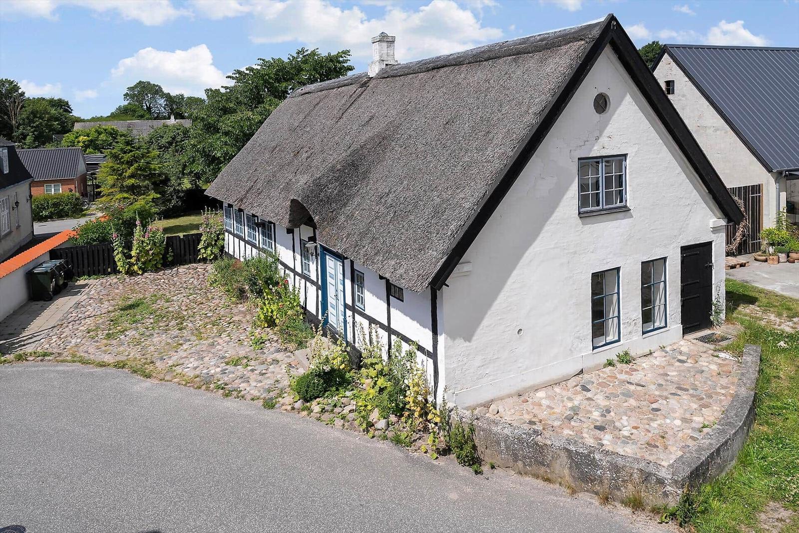 Traditionelles Haus mit Strohdach und weißer Fassade. Garten und Steinweg sichtbar.