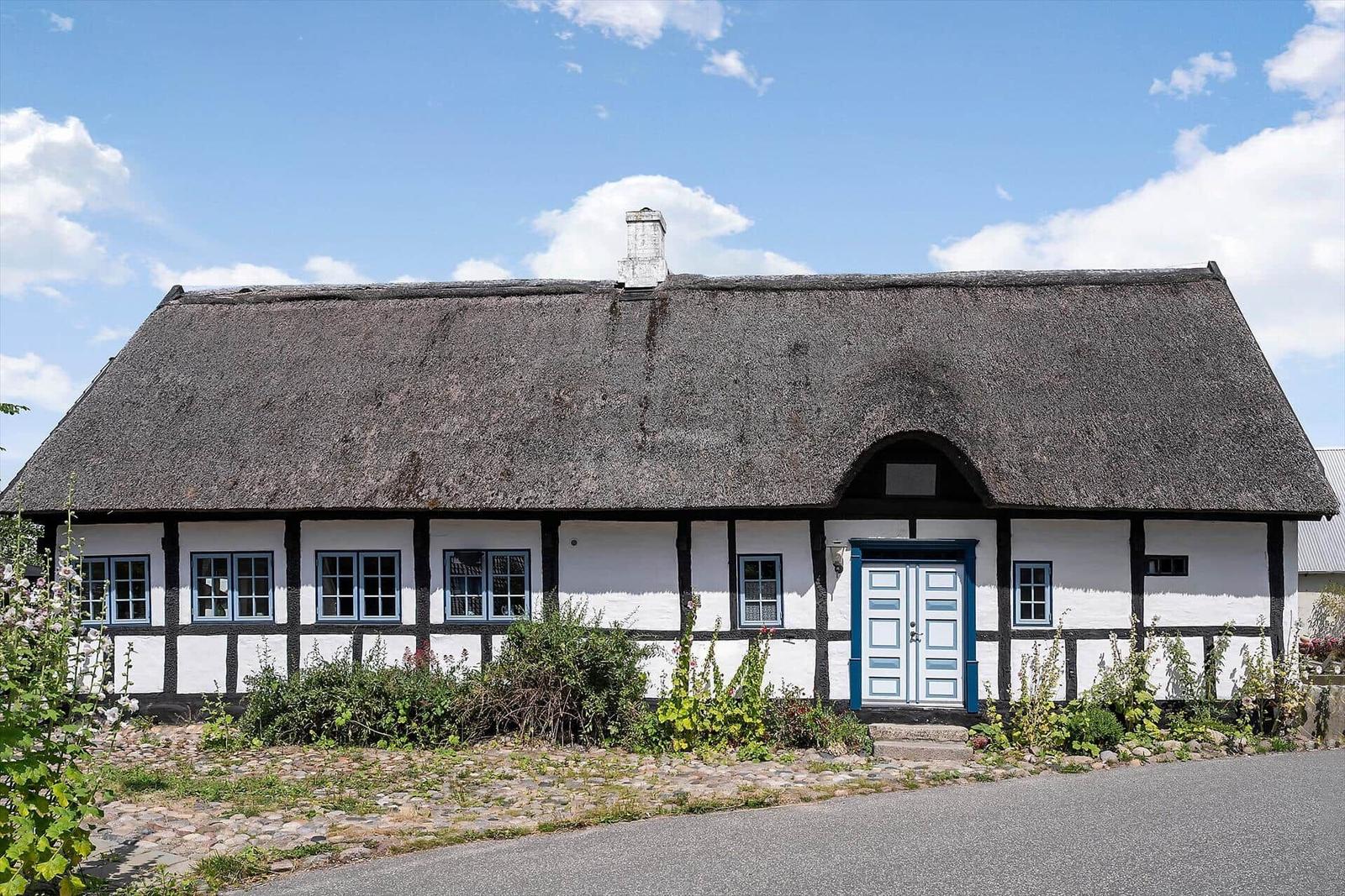 Ein weißes Fachwerkhaus mit strohgedecktem Dach und blauer Tür.
