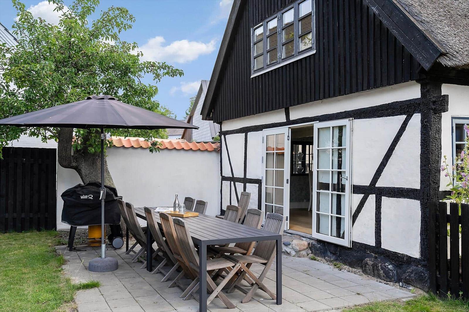 Terrasse mit Tisch, Stühlen und Sonnenschutz vor einem Fachwerkhaus.