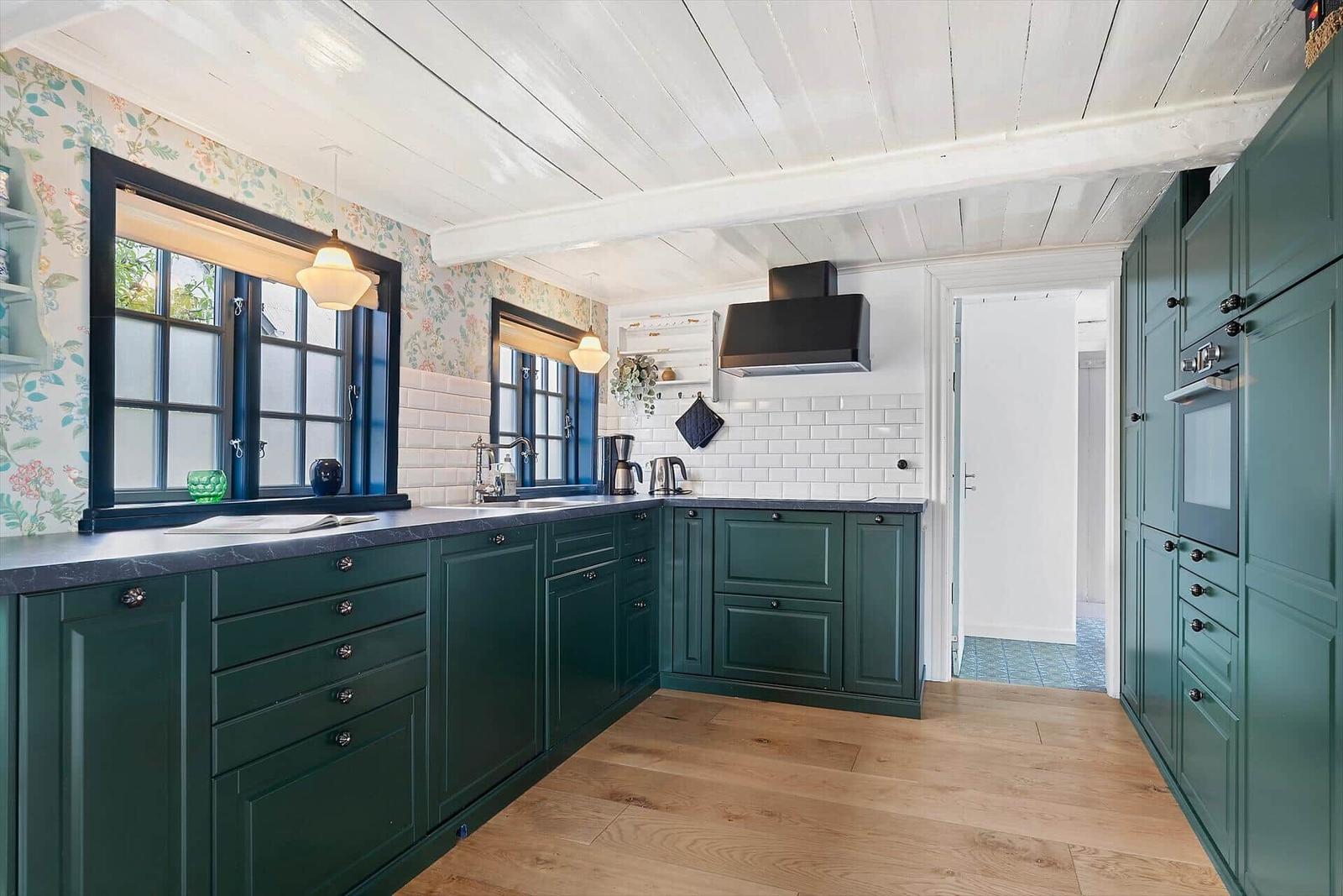 Küche mit grünen Schränken, Holzboden und Fenstern mit Blumenpapier.