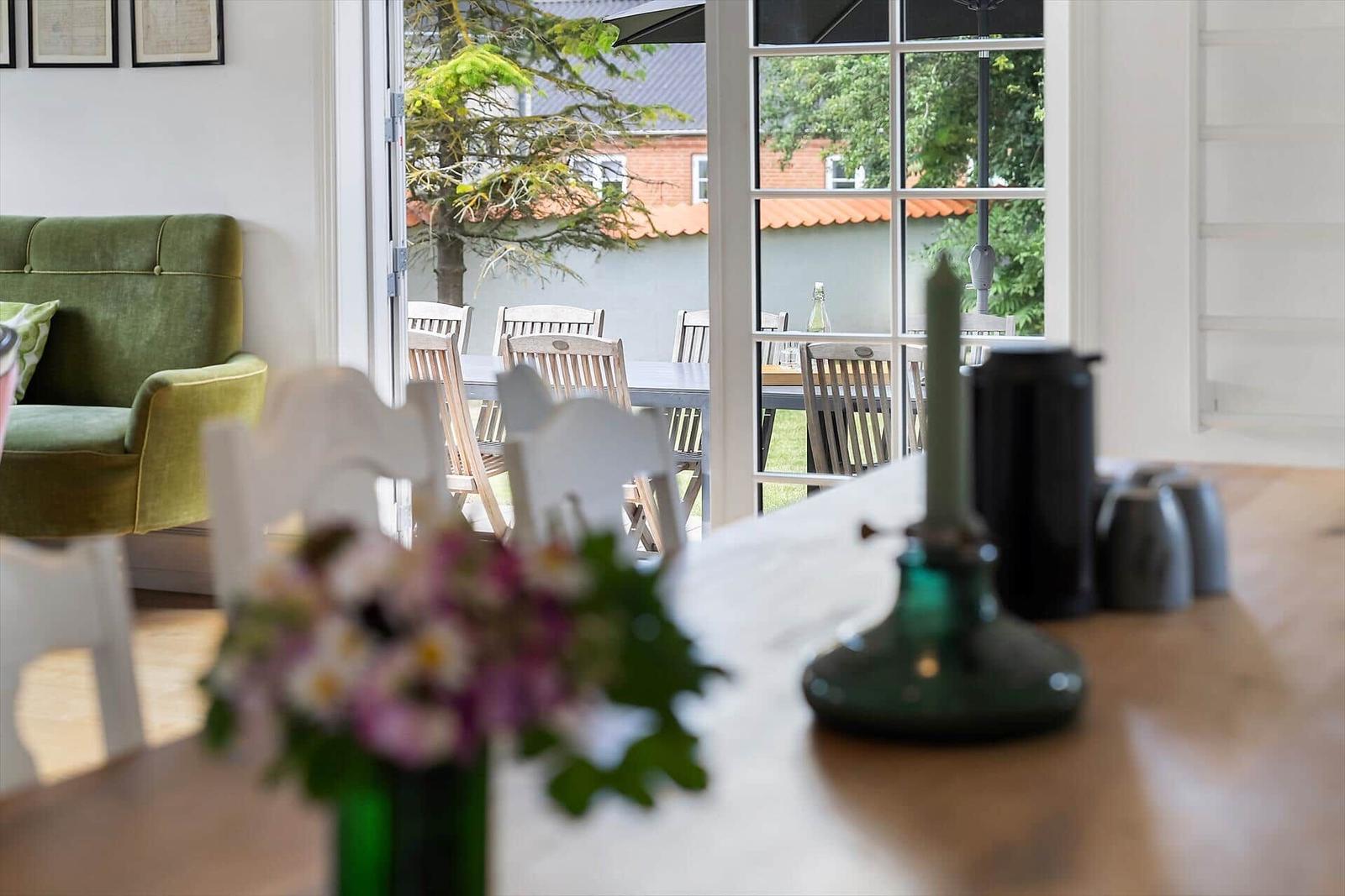 Ein Essbereich mit Tisch und Stühlen. Durch Fenster ist ein Garten mit Tisch und Stühlen sichtbar.
