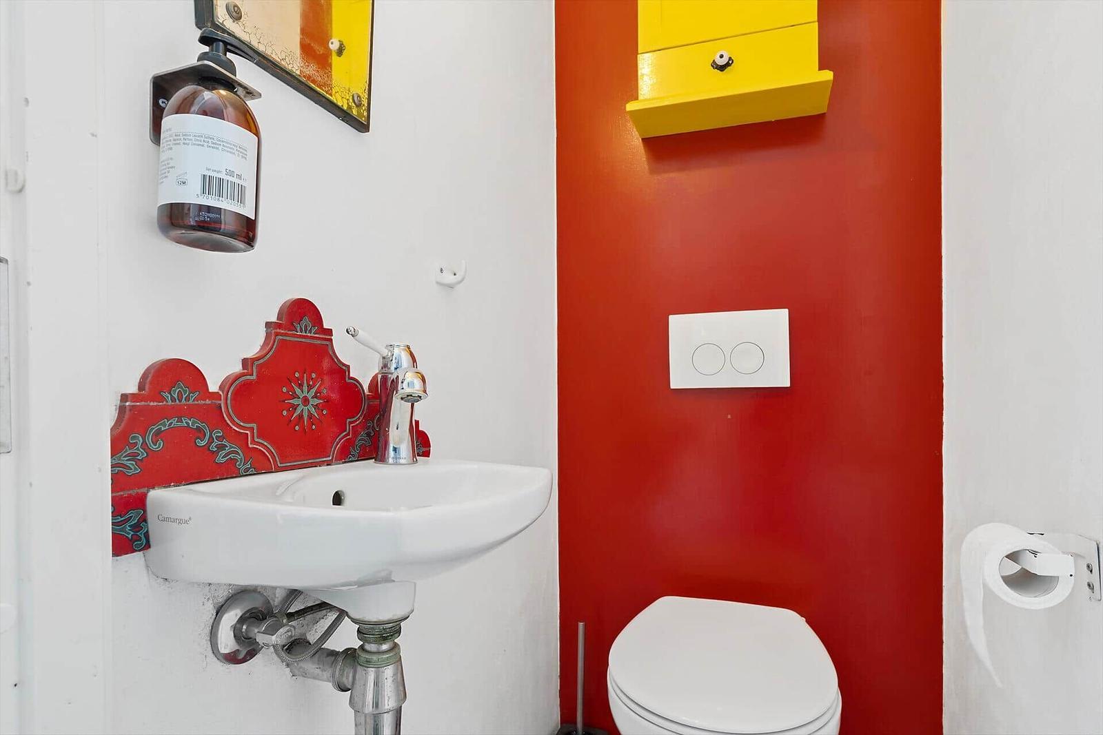 Bad mit Waschbecken, Toilette und gelbem Schrank an roter Wand.