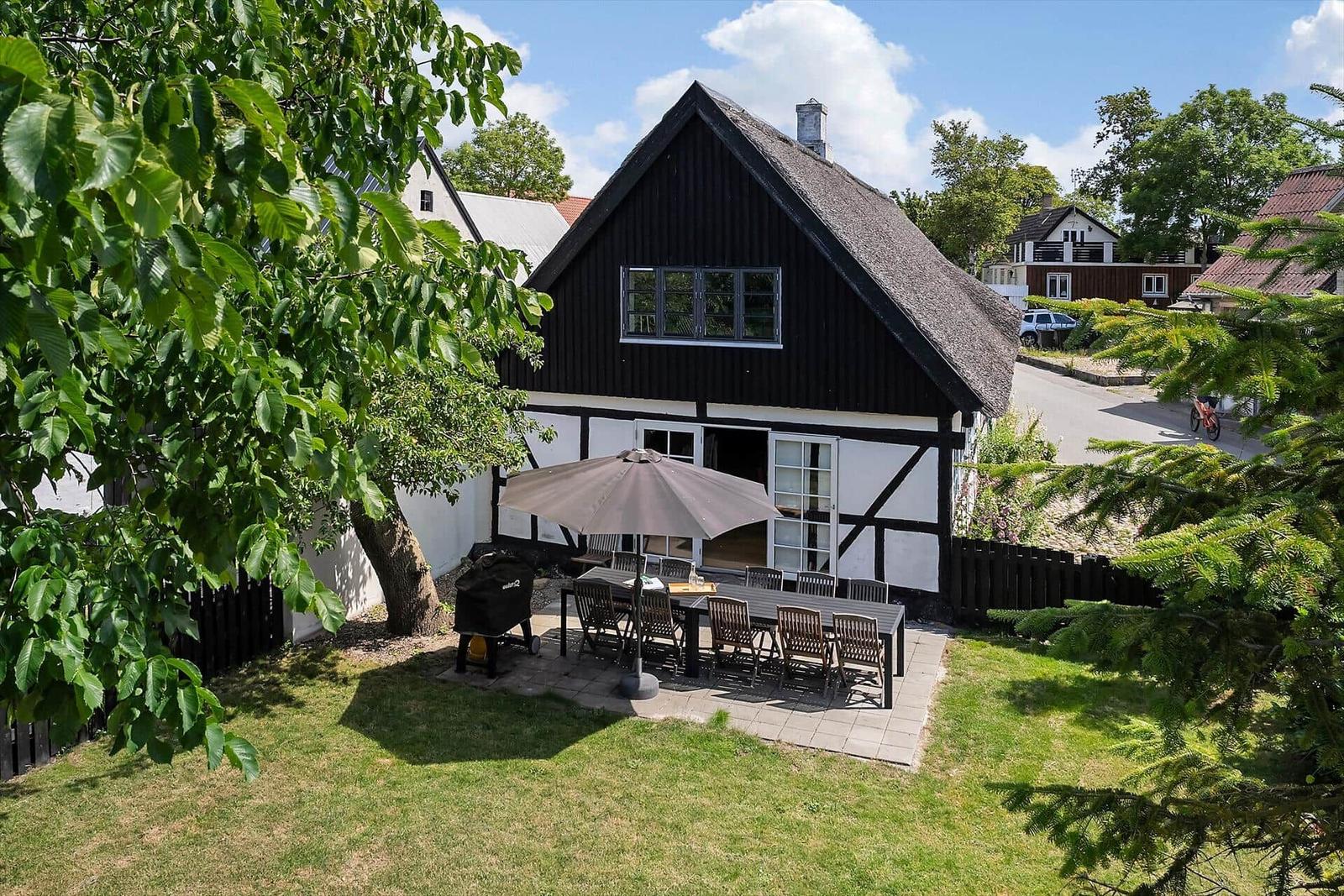 Schwarzes Fachwerkhaus mit strohgedecktem Dach und großer Terrasse mit Tisch, Stühlen und Sonnenschirm.