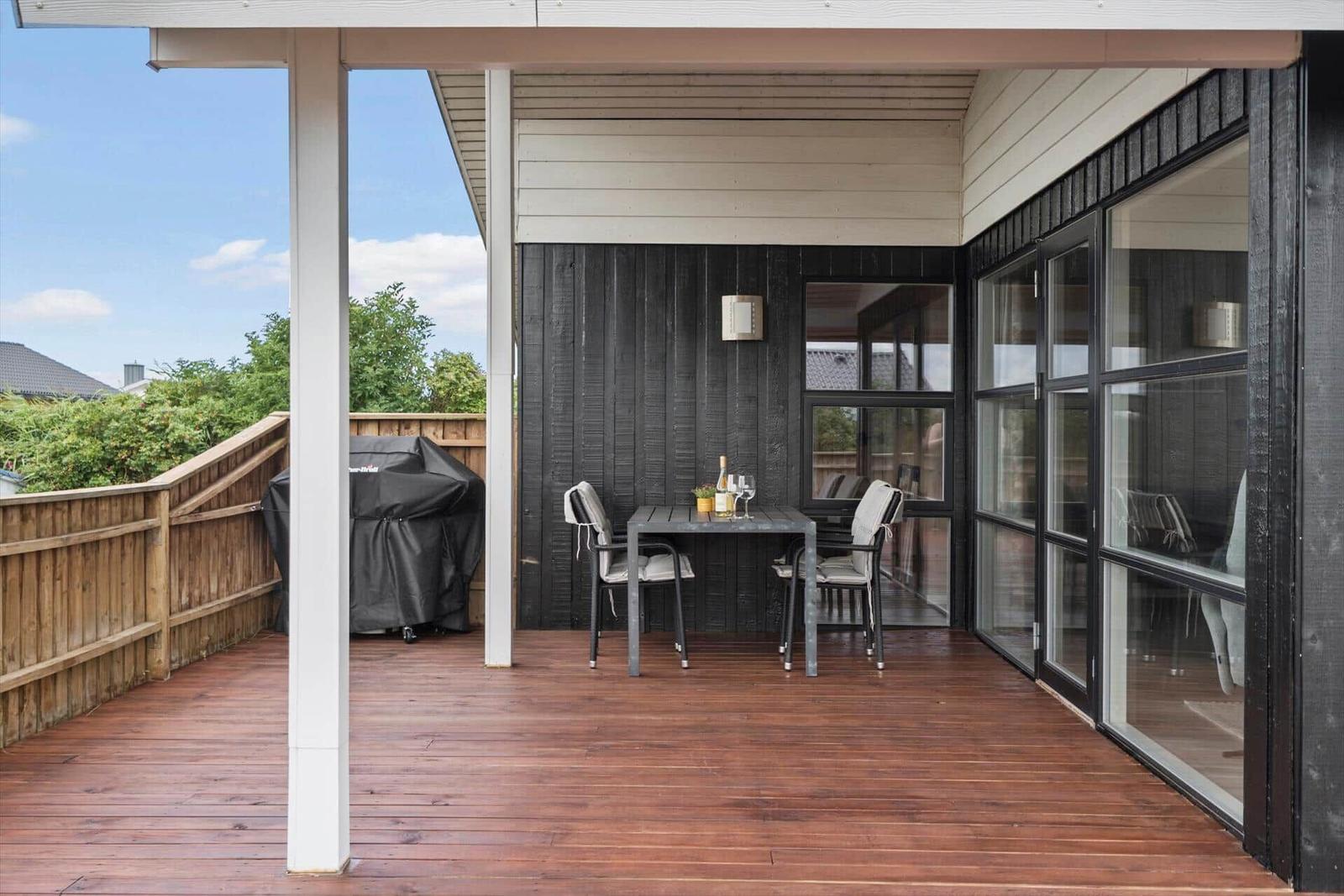 Terrasse mit Tisch, Stühlen und Grill. Holzdecke und Glaswände.