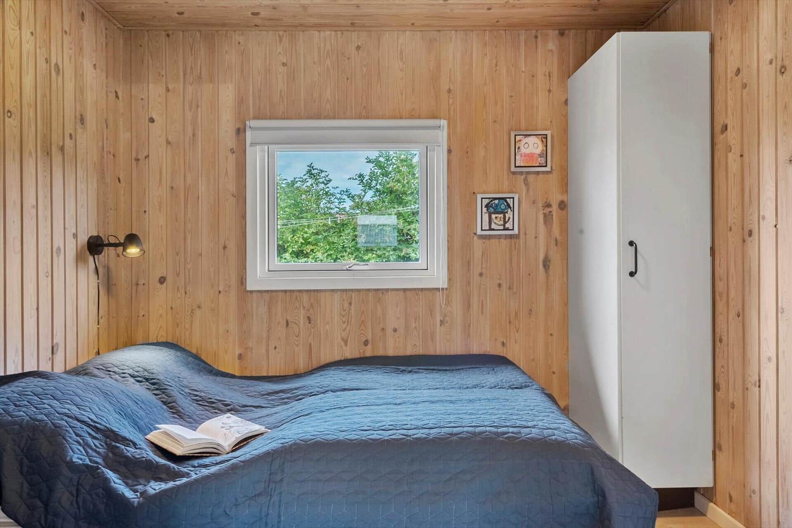 Schlafzimmer mit Holzwand, Bett, Fenster und Kleiderschrank.