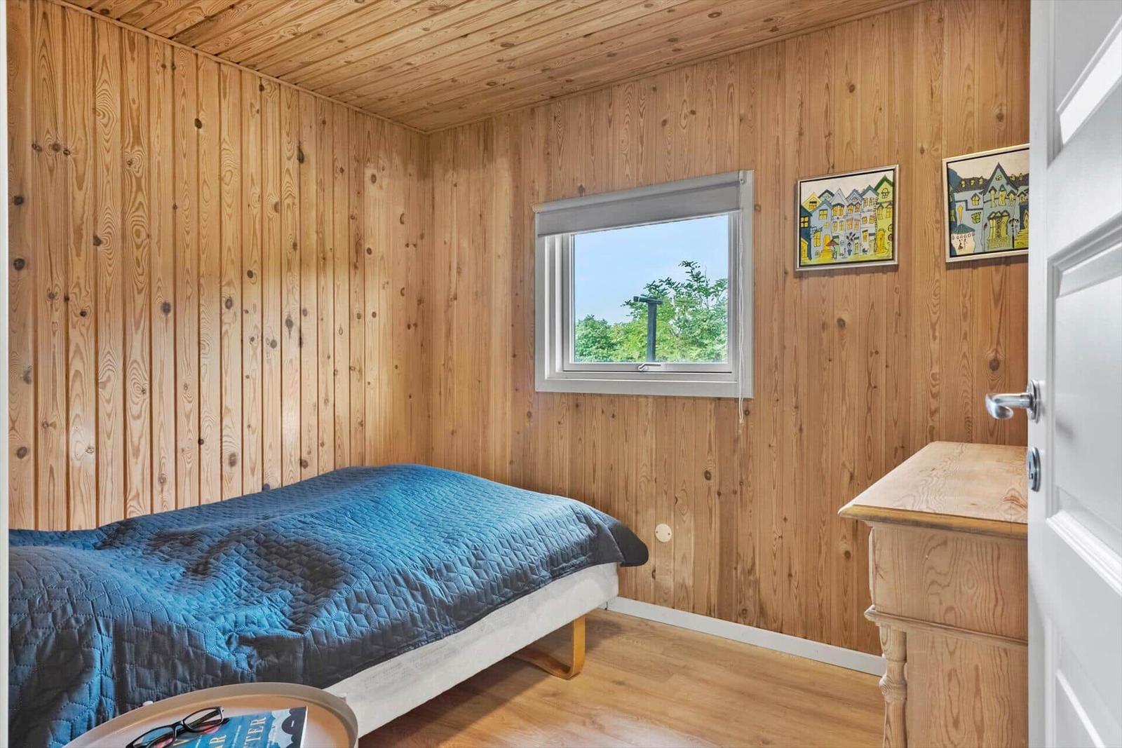 Schlafzimmer mit Holzwand, Bett, Fenster und Schrank.