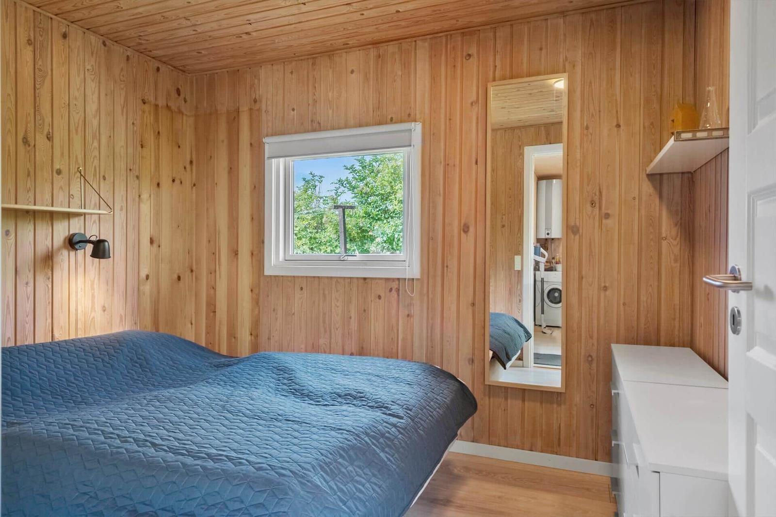 Schlafzimmer mit Holzwänden, Bett und Fenster zum Grün.