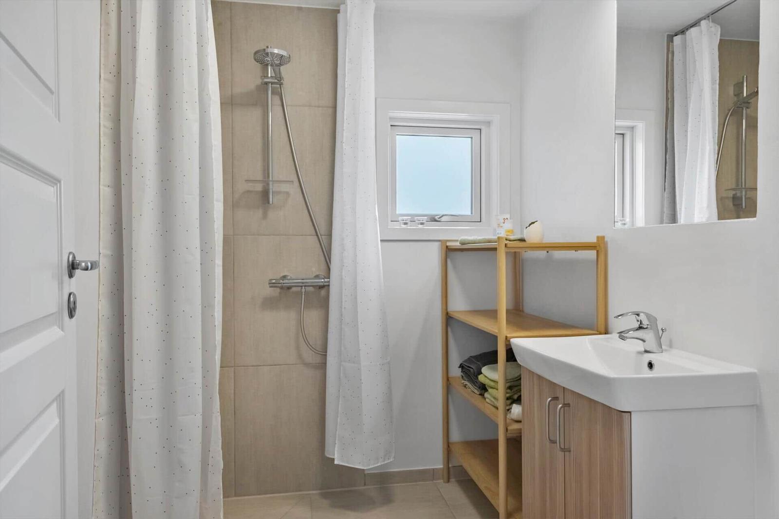 Badezimmer mit Dusche, Waschbecken und Holzregal.