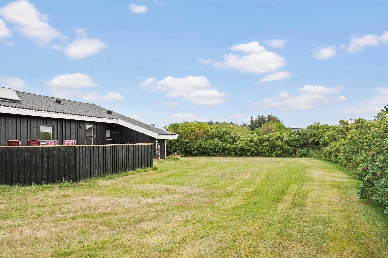 Schwarzes Haus mit Garten und Zaun unter blauem Himmel.