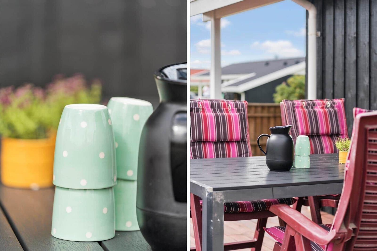 Terrasse mit Tisch, Stühlen und Tassen. Hintergrund: Haus und Himmel.