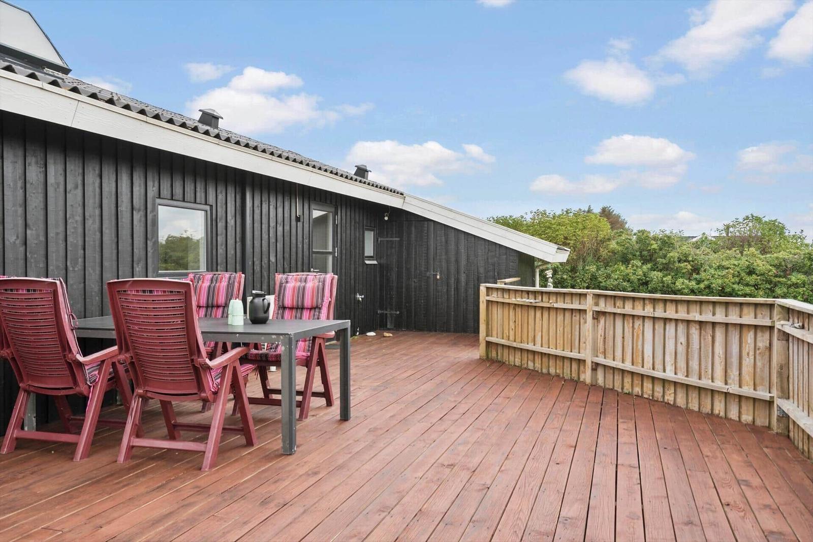Terrasse mit Tisch und Stühlen vor einem Haus mit Holzwand.