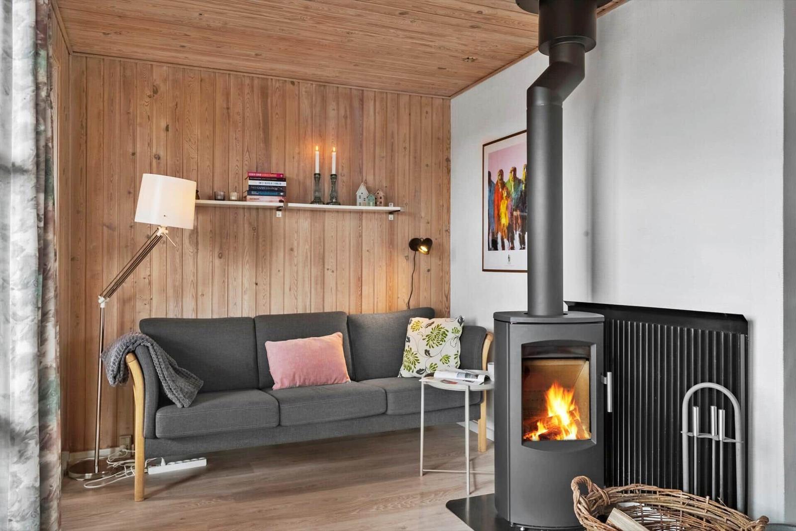 Ein Wohnzimmer mit Sofa, Kamin und Holzwand. Auf einem Regal stehen Bücher und Kerzen.