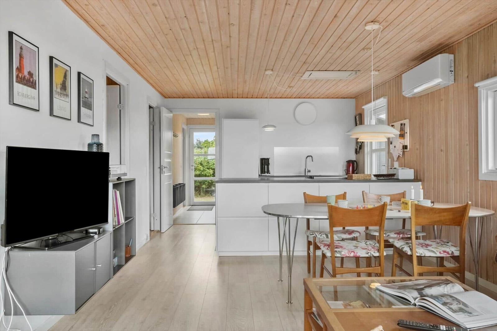 Wohnküche mit Esstisch, TV und Holzdecke.