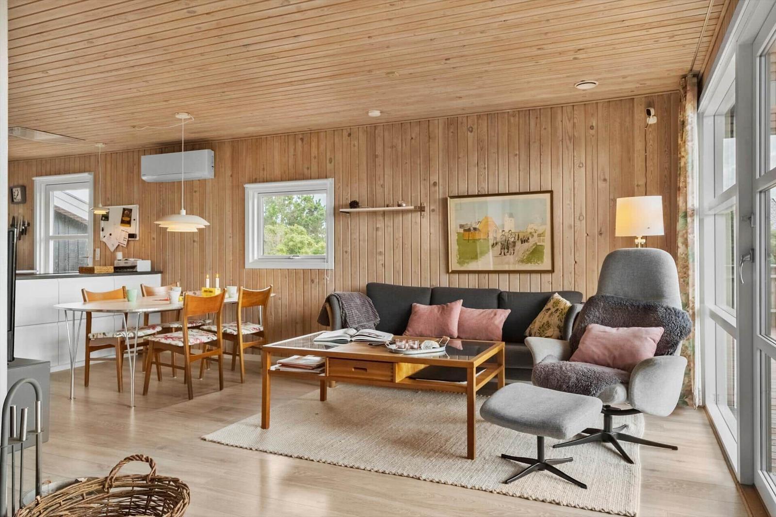 Wohn- und Essbereich mit Holzwand, Sofa, Sessel und Esstisch.
