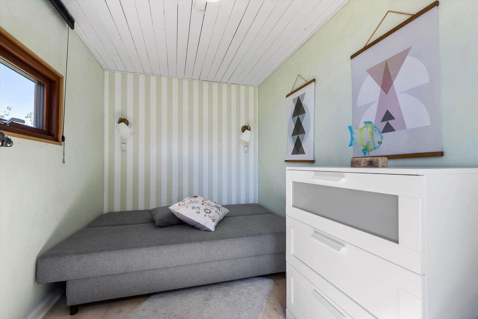 Ein Schlafzimmer mit grauem Bett, weißem Schrank und Streifenwand.