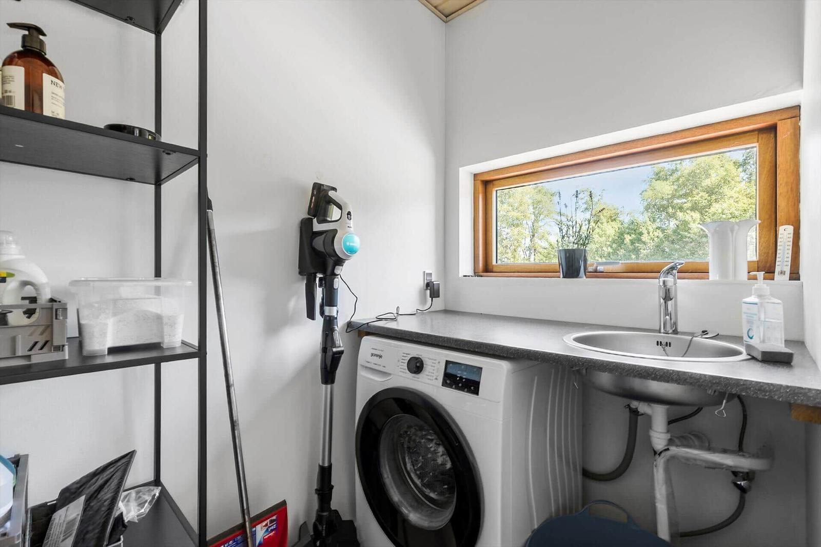 Wäscheschrank mit Waschmaschine, Spüle und Fenster mit Blick auf Grün.