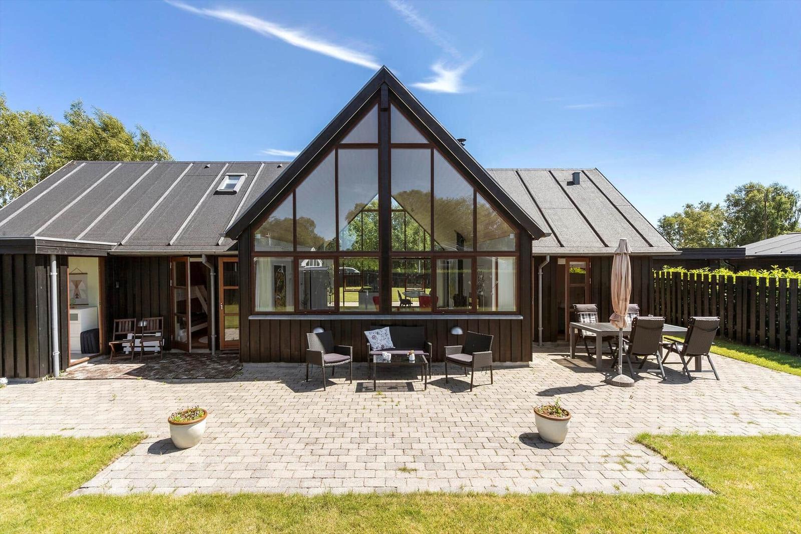 Modernes Haus mit großem Glasbereich und gepflastertem Hof mit Gartenmöbeln.