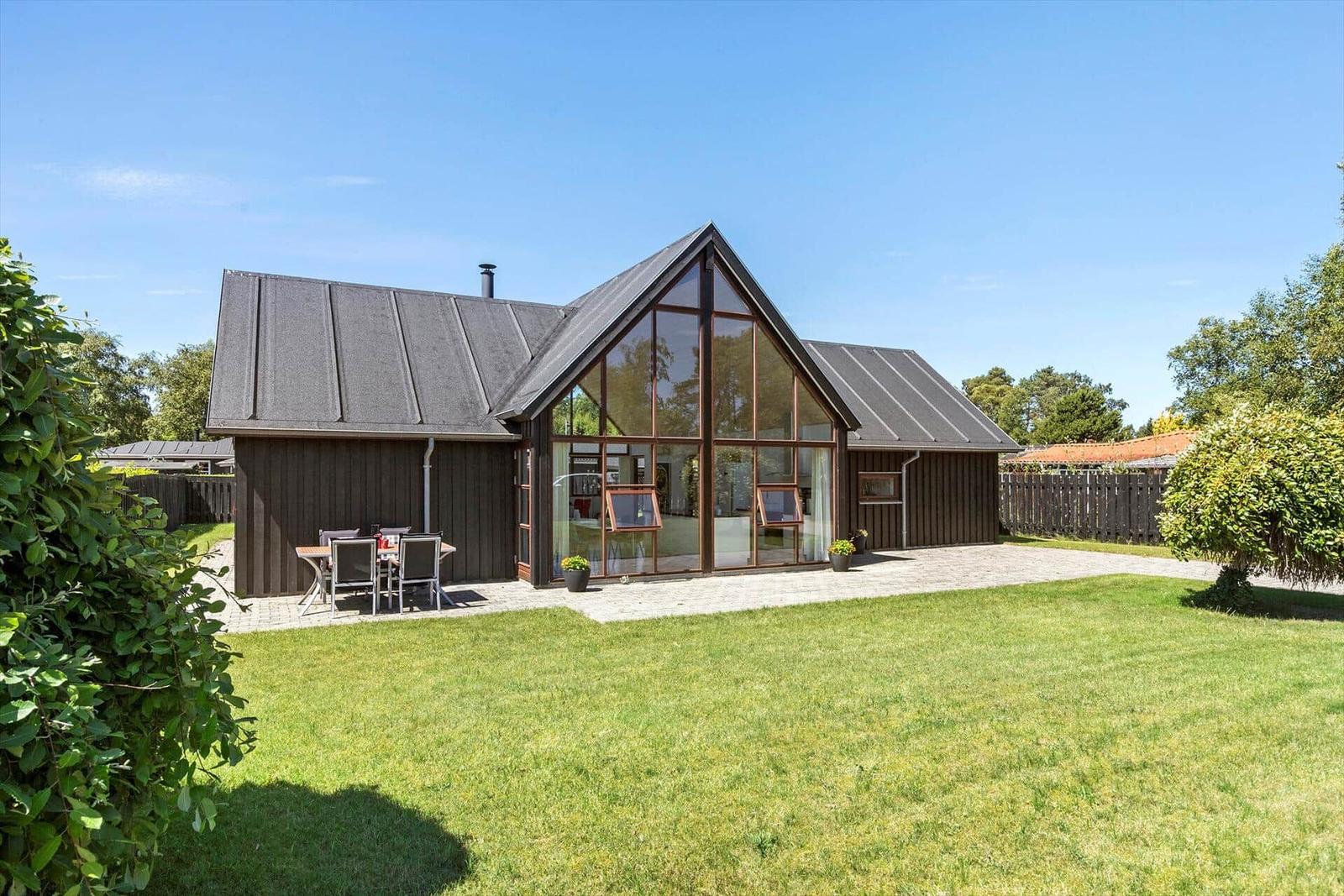 Moderne Villa mit großem Glasbereich und gepflegtem Garten. Außentisch mit Sitzgelegenheit.