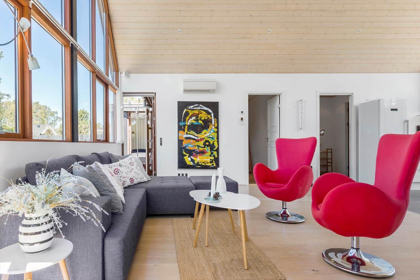 Wohnzimmer mit grauem Sofa, zwei roten Stühlen und großem Fenster.