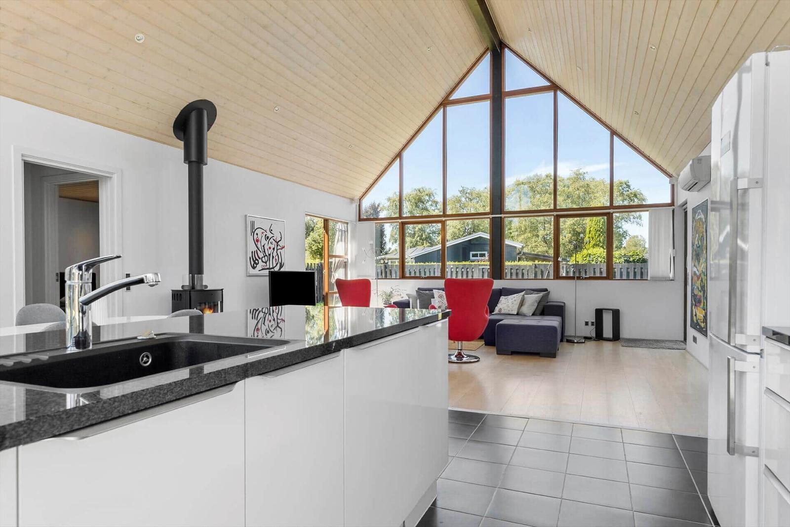 Küche mit Blick auf Wohnbereich mit rotem Sessel und großem Fenster