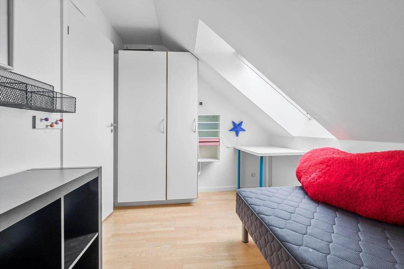 Schlafzimmer mit Dachschräge, Bett, Schrank und Schreibtisch.