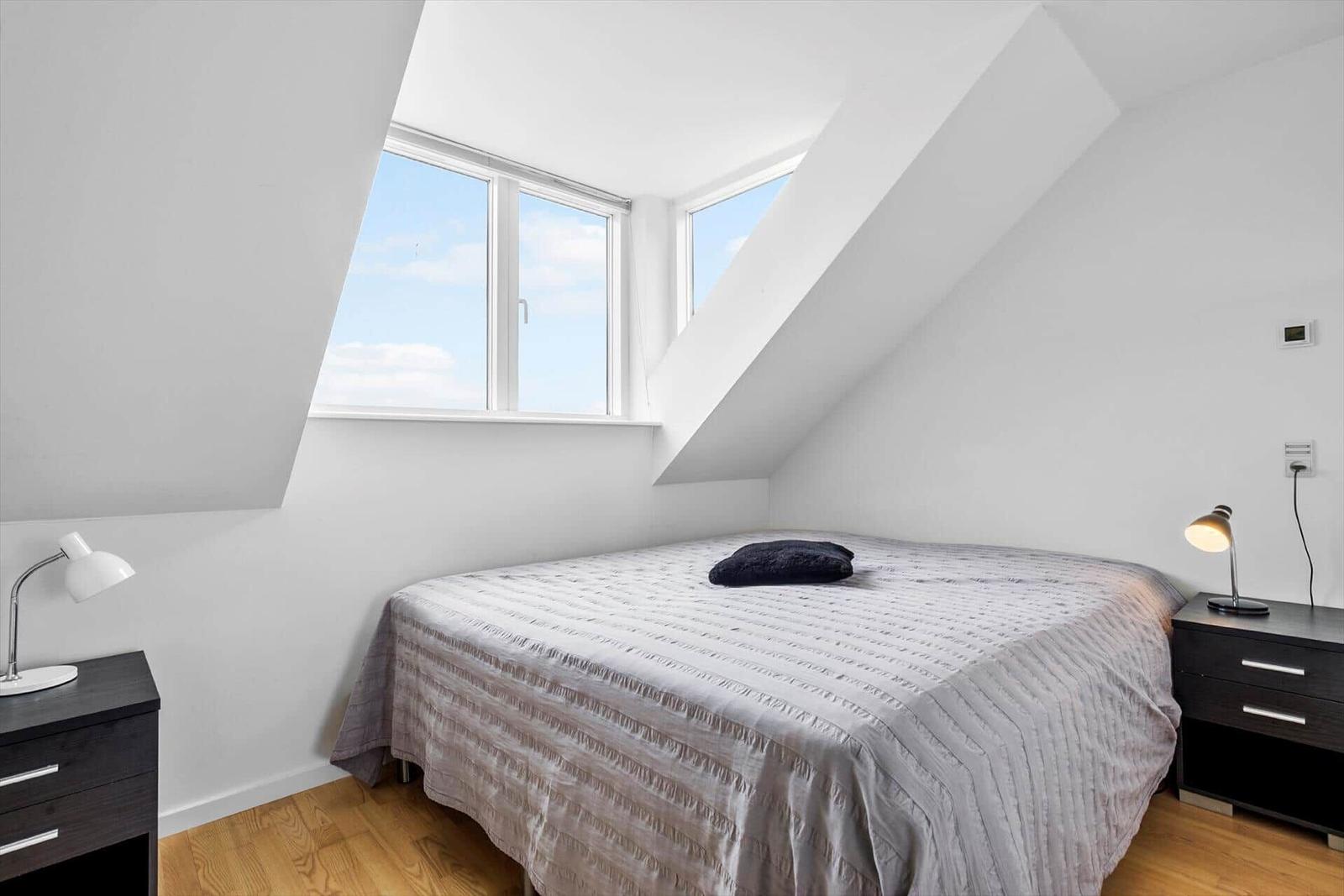Schlafzimmer mit Dachschrägen, großem Fenster und zwei Nachttischen mit Lampen.