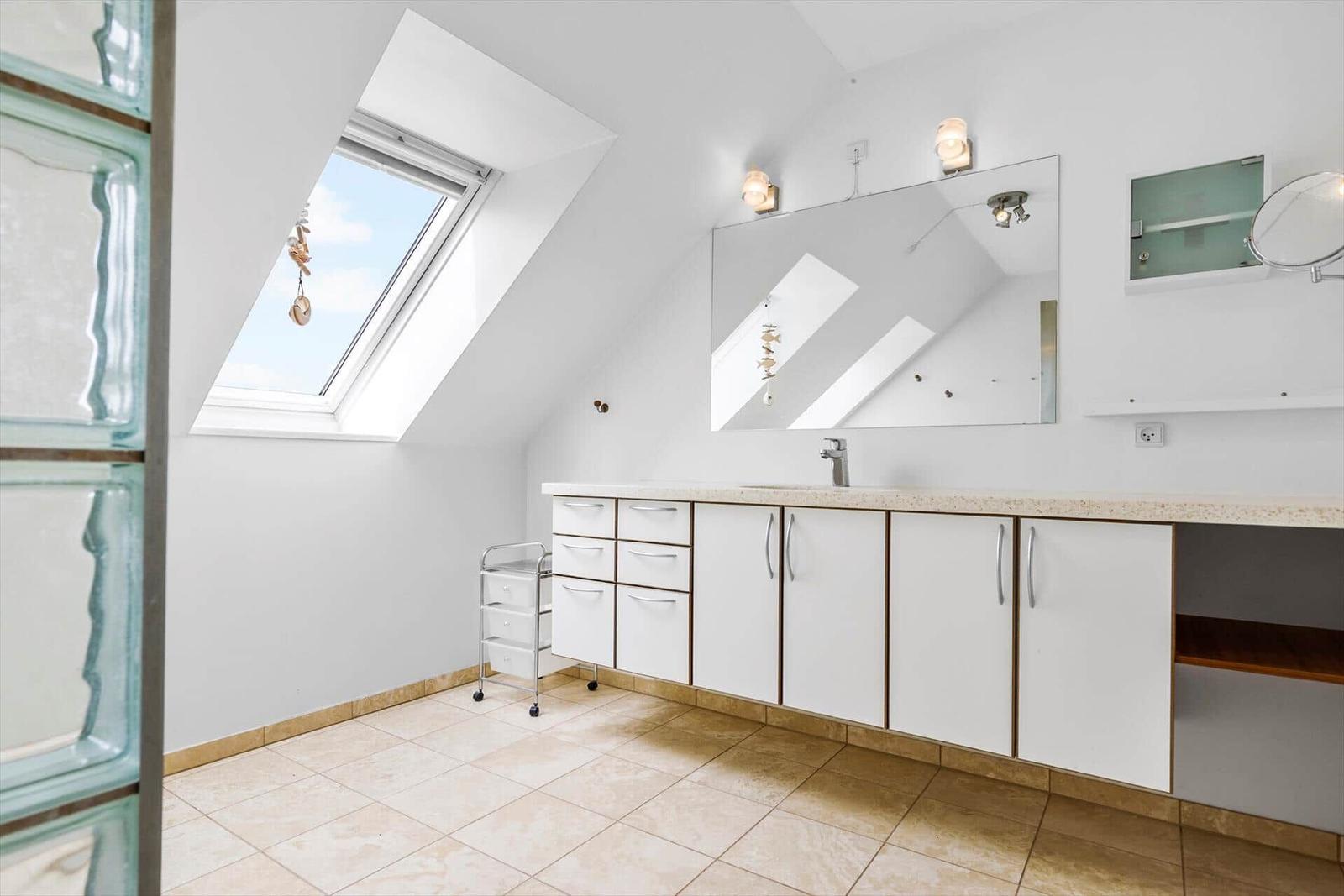 Badezimmer mit Dachschrägen, Fenster, Spiegel und Waschtisch.